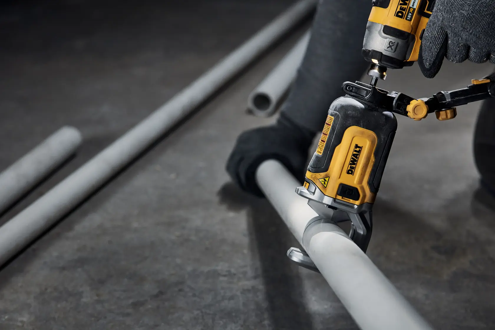 Nærbilde av et DEWALT elektrisk verktøy brukt av en person med hansker for å kutte et grått metallrør på verkstedsgulvet.